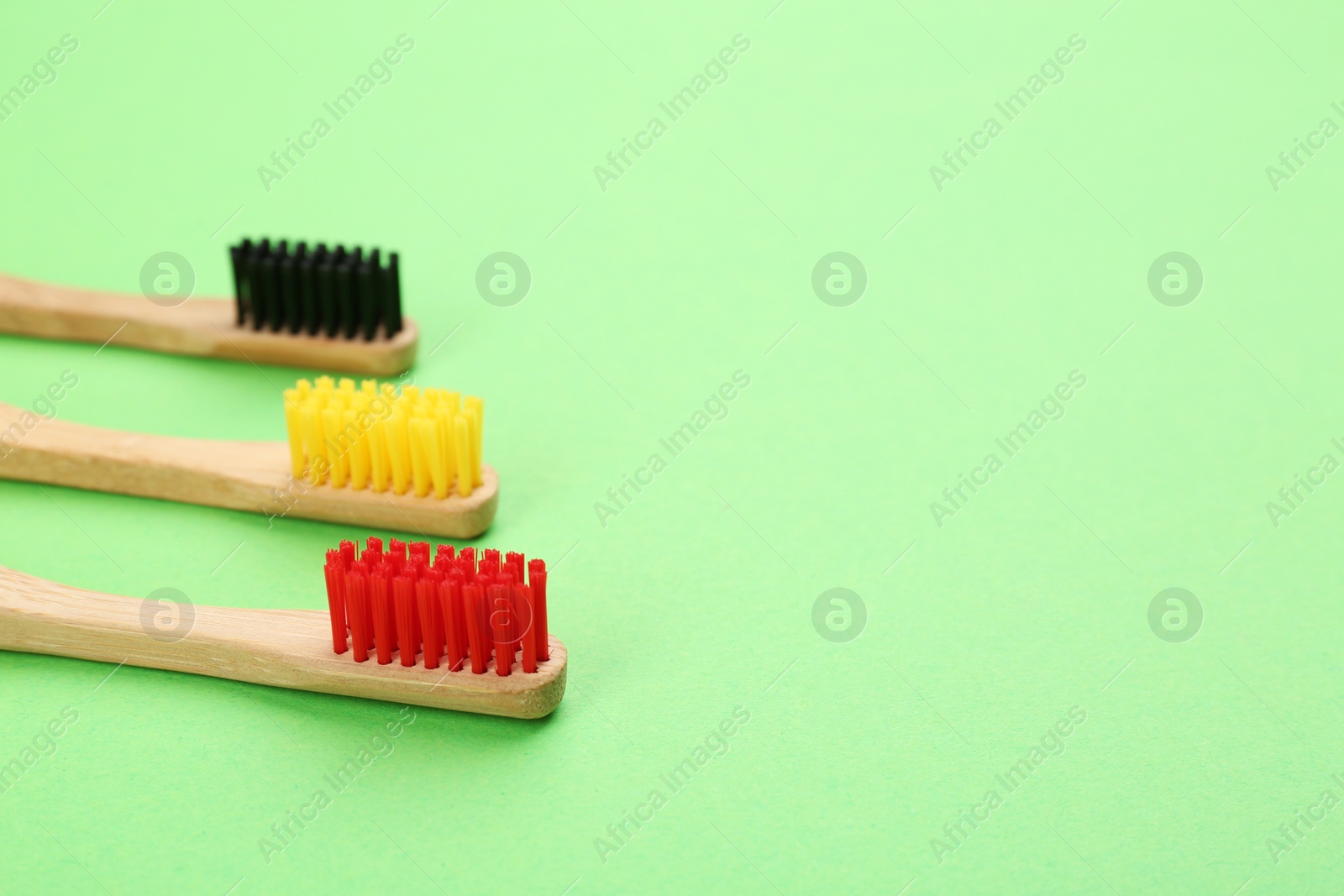 Photo of Natural bamboo toothbrushes on green background. Space for text
