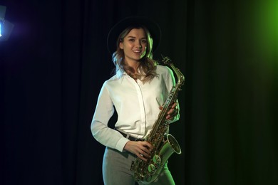 Photo of Beautiful young woman with saxophone on dark background