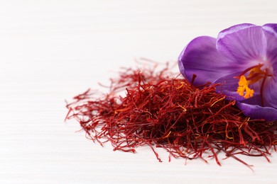 Photo of Dried saffron and crocus flower on white wooden table, closeup. Space for text