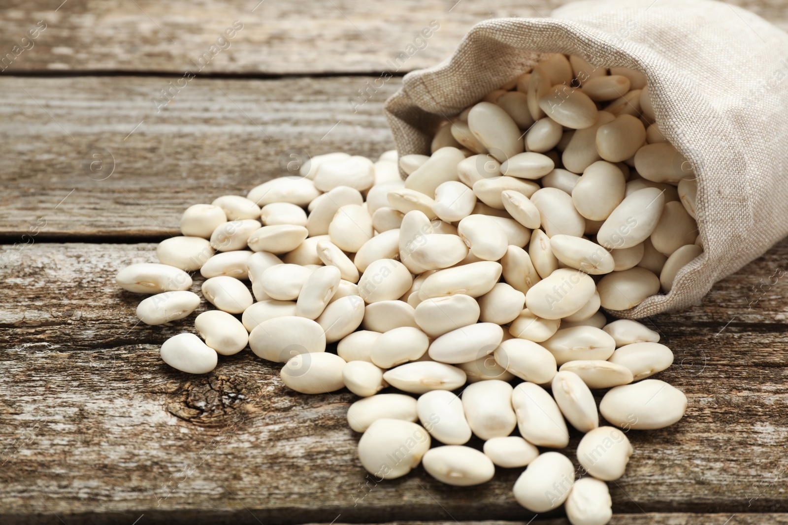 Photo of Overturned sack with white beans on wooden table, closeup