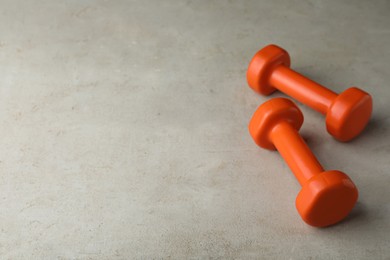 Photo of Orange vinyl dumbbells on light grey table. Space for text