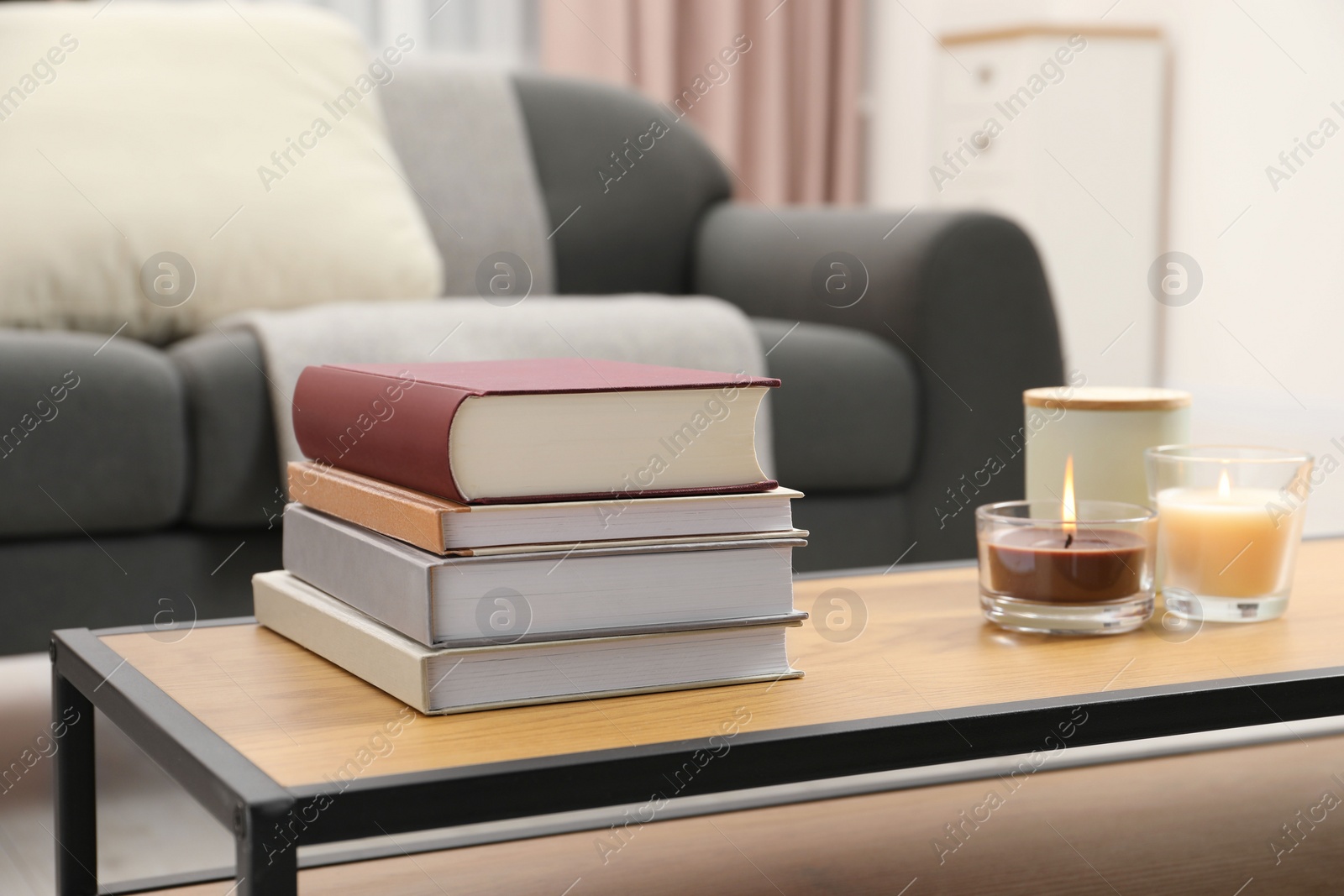 Photo of Books and burning candles on wooden table in living room