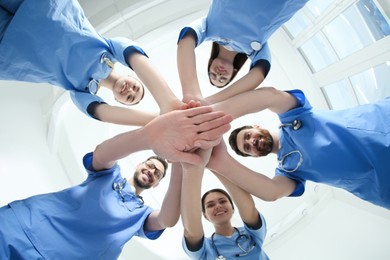 Photo of Young doctors stacking hands together indoors, bottom view