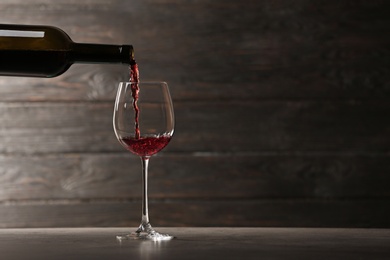 Photo of Pouring red wine into glass from bottle on table against wooden background. Space for text