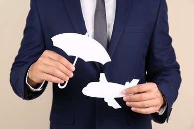 Photo of Insurance agent covering paper plane with umbrella cutout on color background, closeup. Travel safety concept