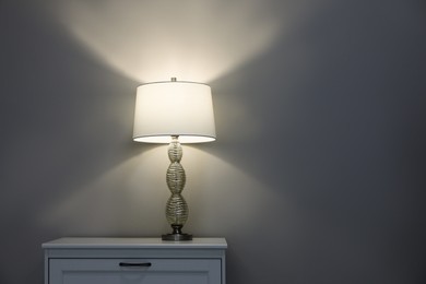 Photo of Wooden nightstand with lamp near wall in room, space for text