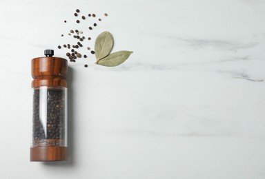 Photo of Pepper shaker and bay leaves on white marble table, flat lay. Space for text