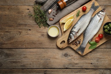 Photo of Sea bass fish and ingredients on wooden table, flat lay. Space for text