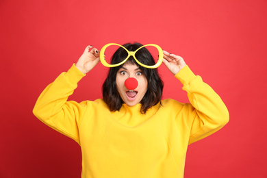 Photo of Emotional woman with large glasses and clown nose on red background. April fool's day