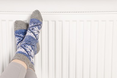 Photo of Woman warming feet near heating radiator, closeup. Space for text