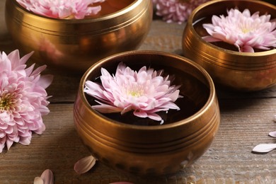Photo of Tibetan singing bowls with water and beautiful flowers on wooden table, closeup