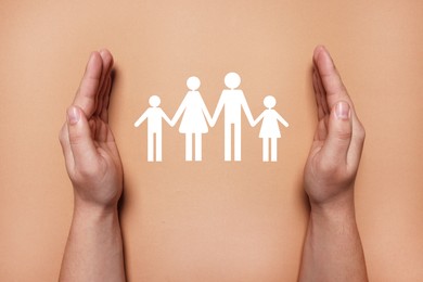 Image of Man holding hands around paper silhouette of family on coral background, top view. Insurance concept