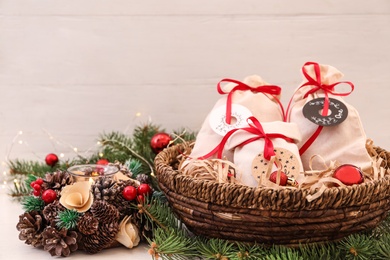Photo of Bags with gifts in basket and festive decor on white table. Christmas advent calendar