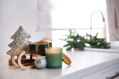 Toy sleigh with gift box, decorative Christmas tree, candle and ball on white countertop indoors