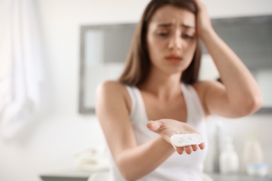 Young woman holding cotton pad with fallen eyelashes indoors