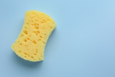 Photo of New yellow sponge on light blue background, top view. Space for text