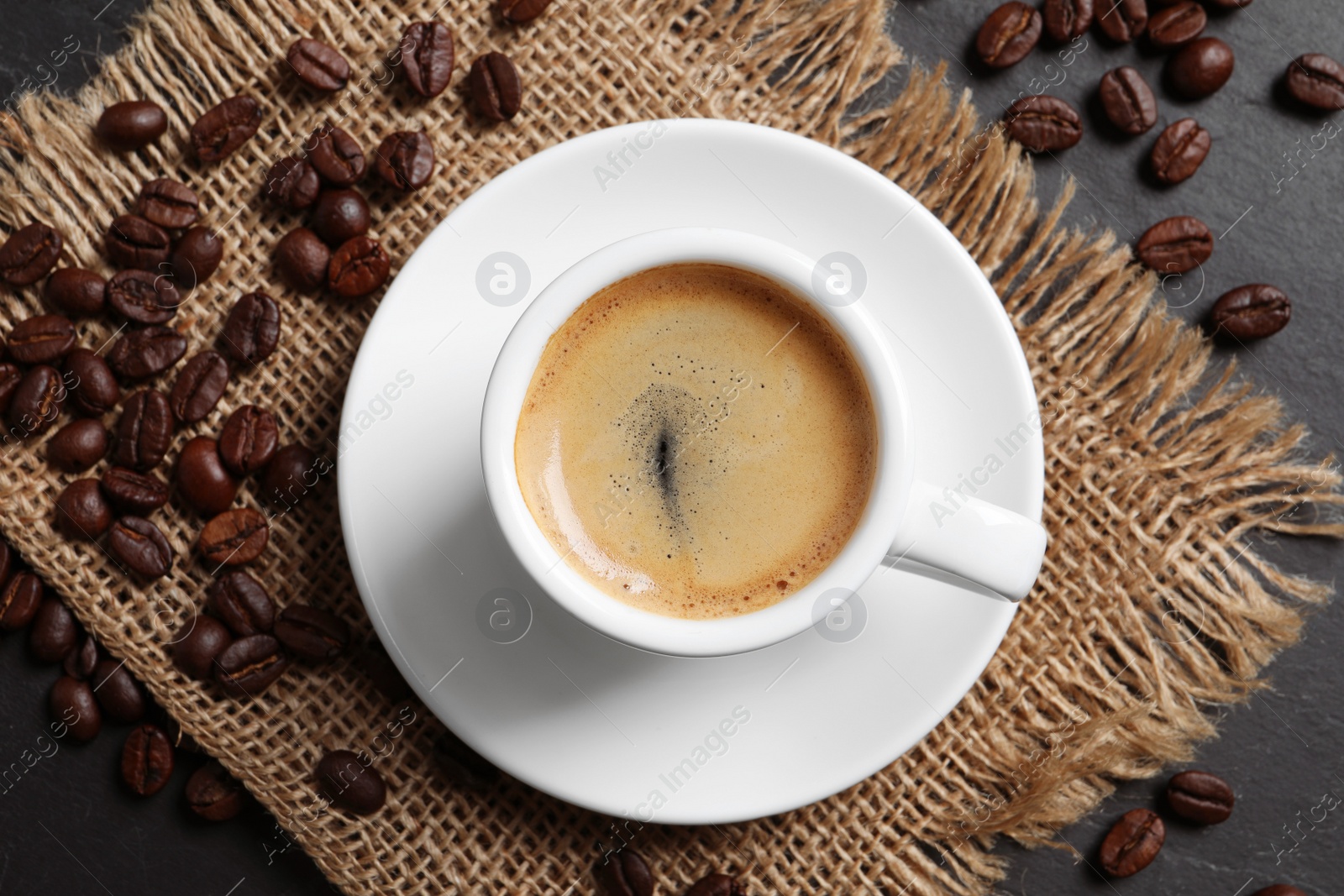 Photo of Cup of hot aromatic coffee and roasted beans on black table, flat lay