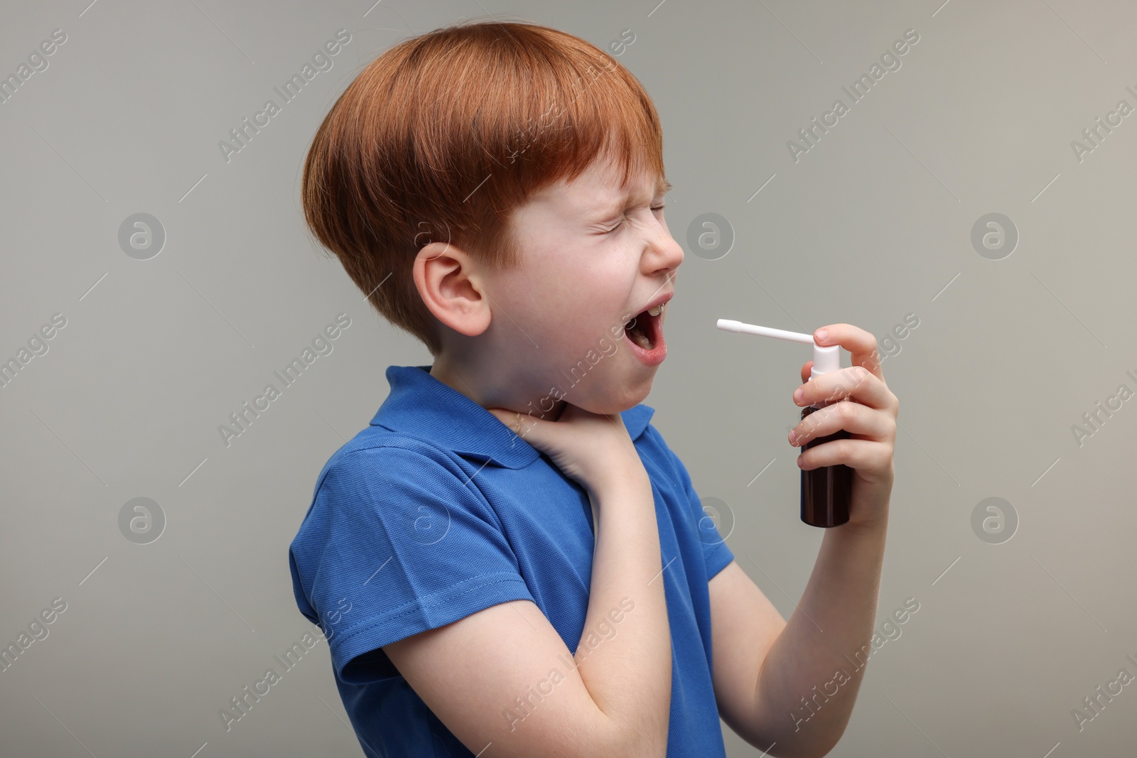 Photo of Little boy using throat spray on grey background