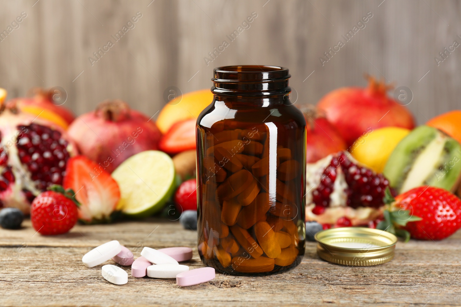 Photo of Vitamin pills, bottle and fresh fruits on wooden table