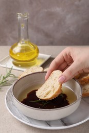 Photo of Woman dipping piece of bread into balsamic vinegar with oil and rosemary at table, closeup