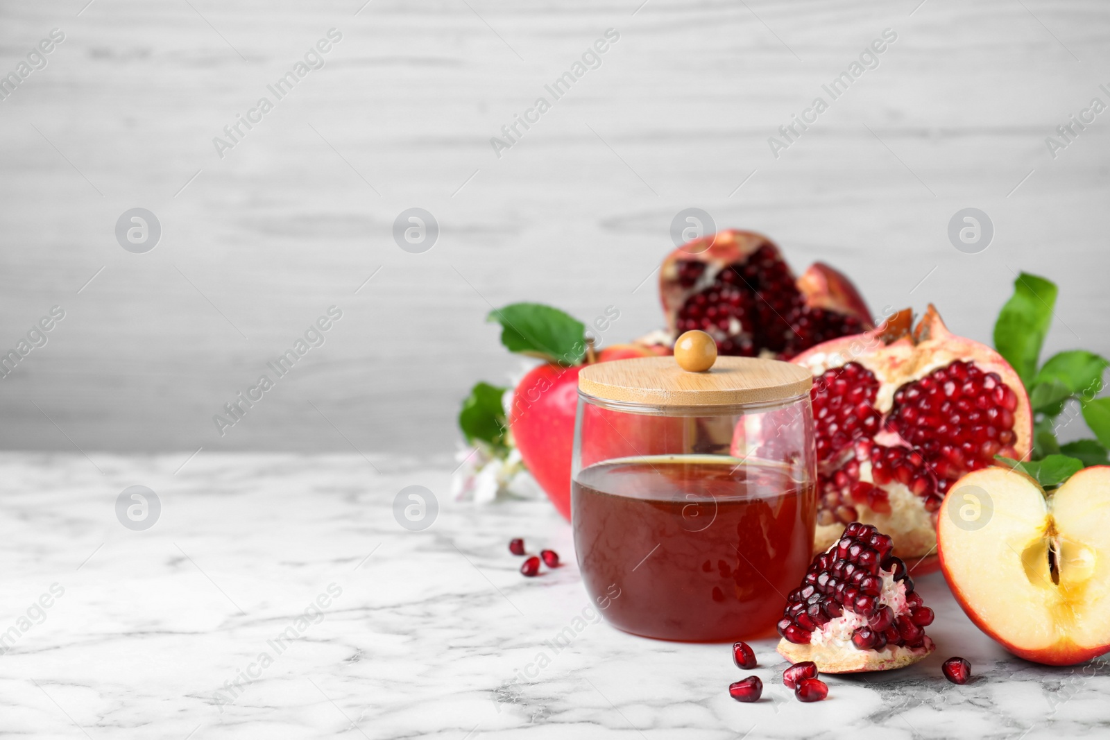 Photo of Honey, pomegranate and apples on white marble table, space for text. Rosh Hashana holiday