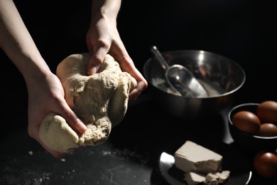 Photo of Making bread. Woman kneading dough at black table on dark background, closeup. Space for text