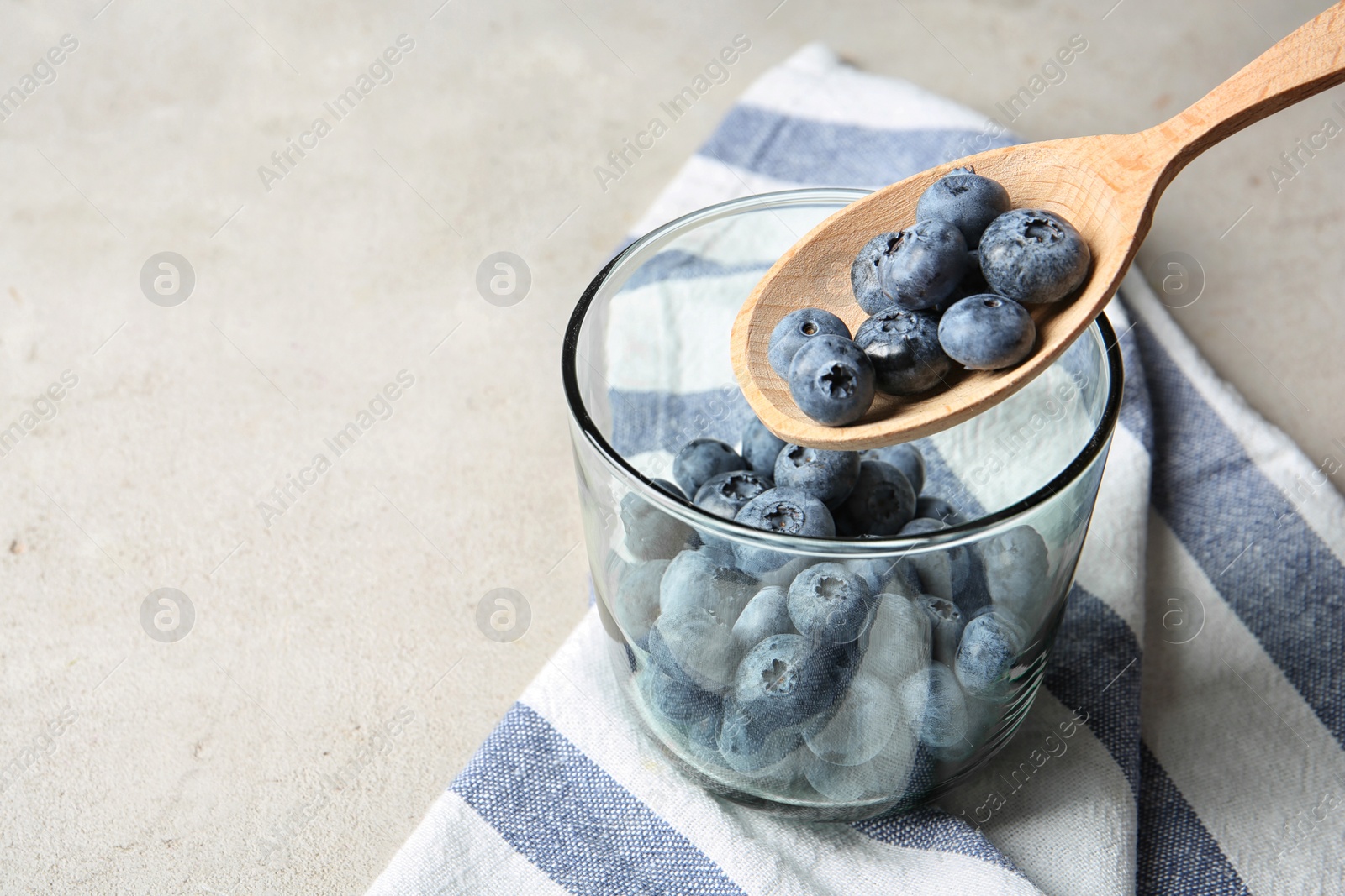 Photo of Spoon with juicy blueberries over glass and space for text on color table