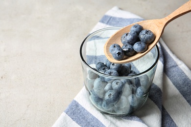 Photo of Spoon with juicy blueberries over glass and space for text on color table