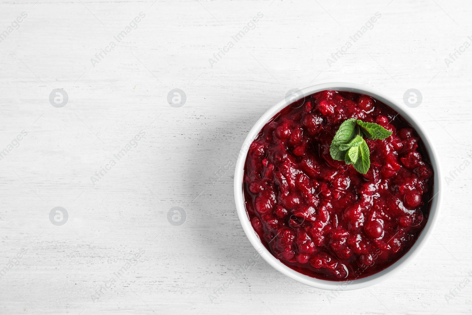 Photo of Bowl of tasty cranberry sauce with sauce on white wooden background, top view. Space for text