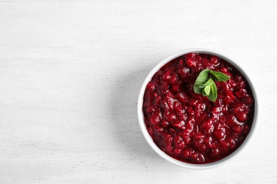 Bowl of tasty cranberry sauce with sauce on white wooden background, top view. Space for text