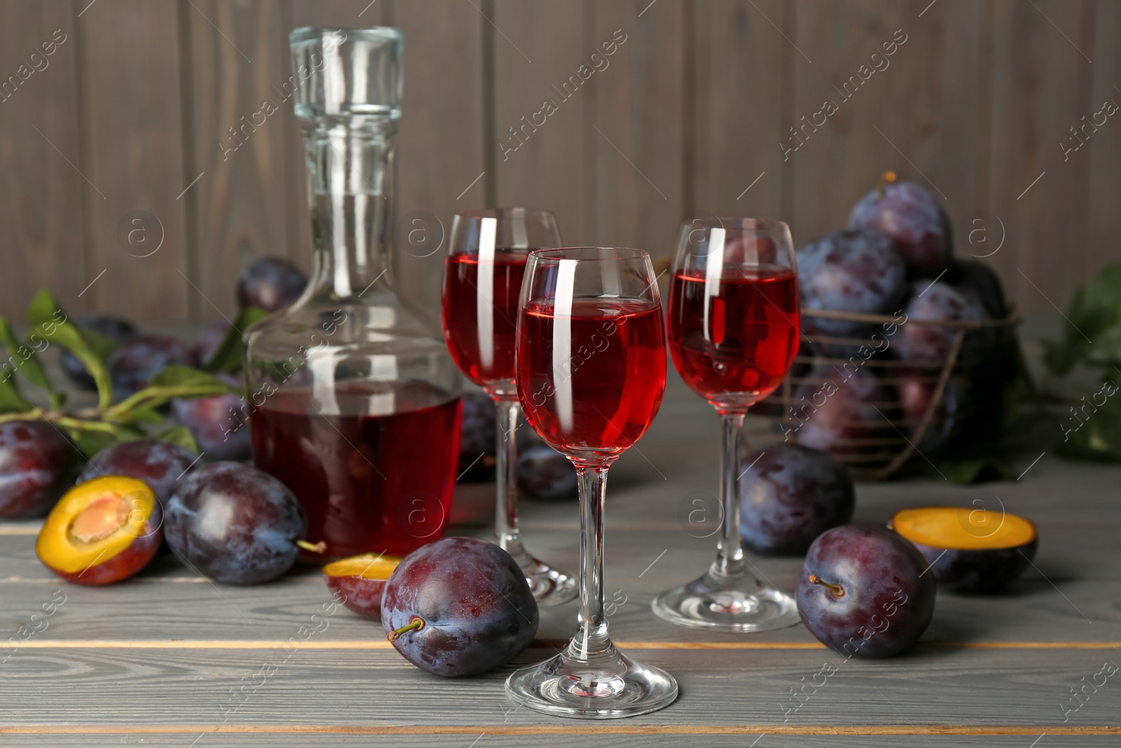 Photo of Delicious plum liquor and ripe fruits on grey wooden table. Homemade strong alcoholic beverage