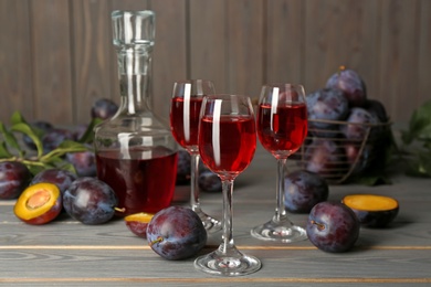 Photo of Delicious plum liquor and ripe fruits on grey wooden table. Homemade strong alcoholic beverage