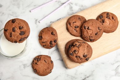 Photo of Wooden board with tasty chocolate chip cookies and milk on table, top view