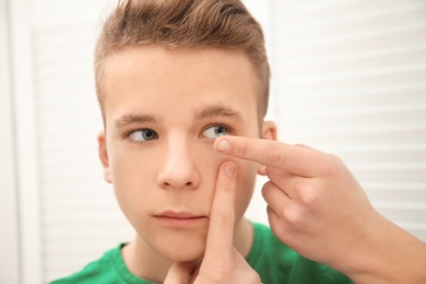 Teenage boy putting contact lens in his eye indoors