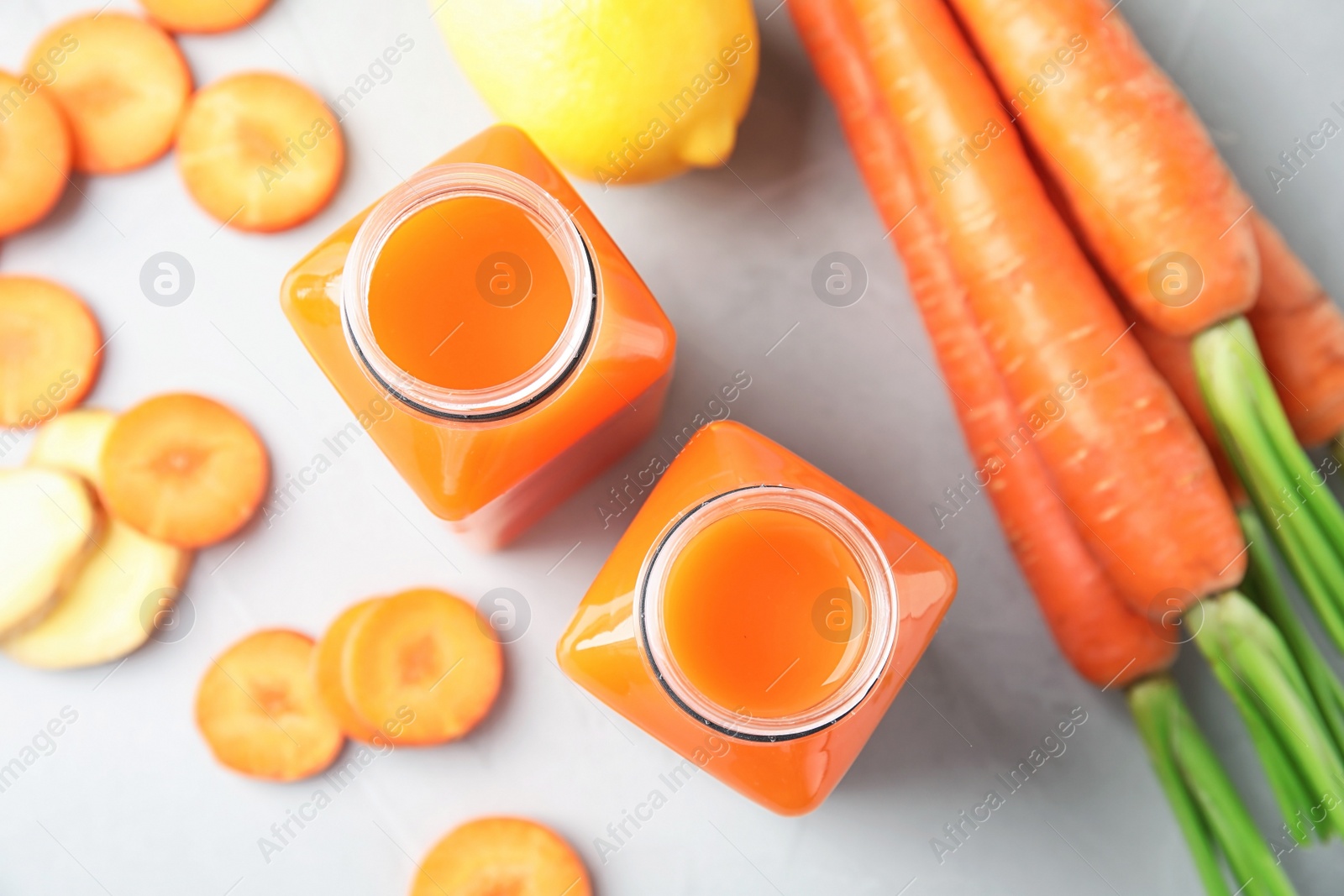 Photo of Bottles with carrot juice and fresh ingredients on table, top view