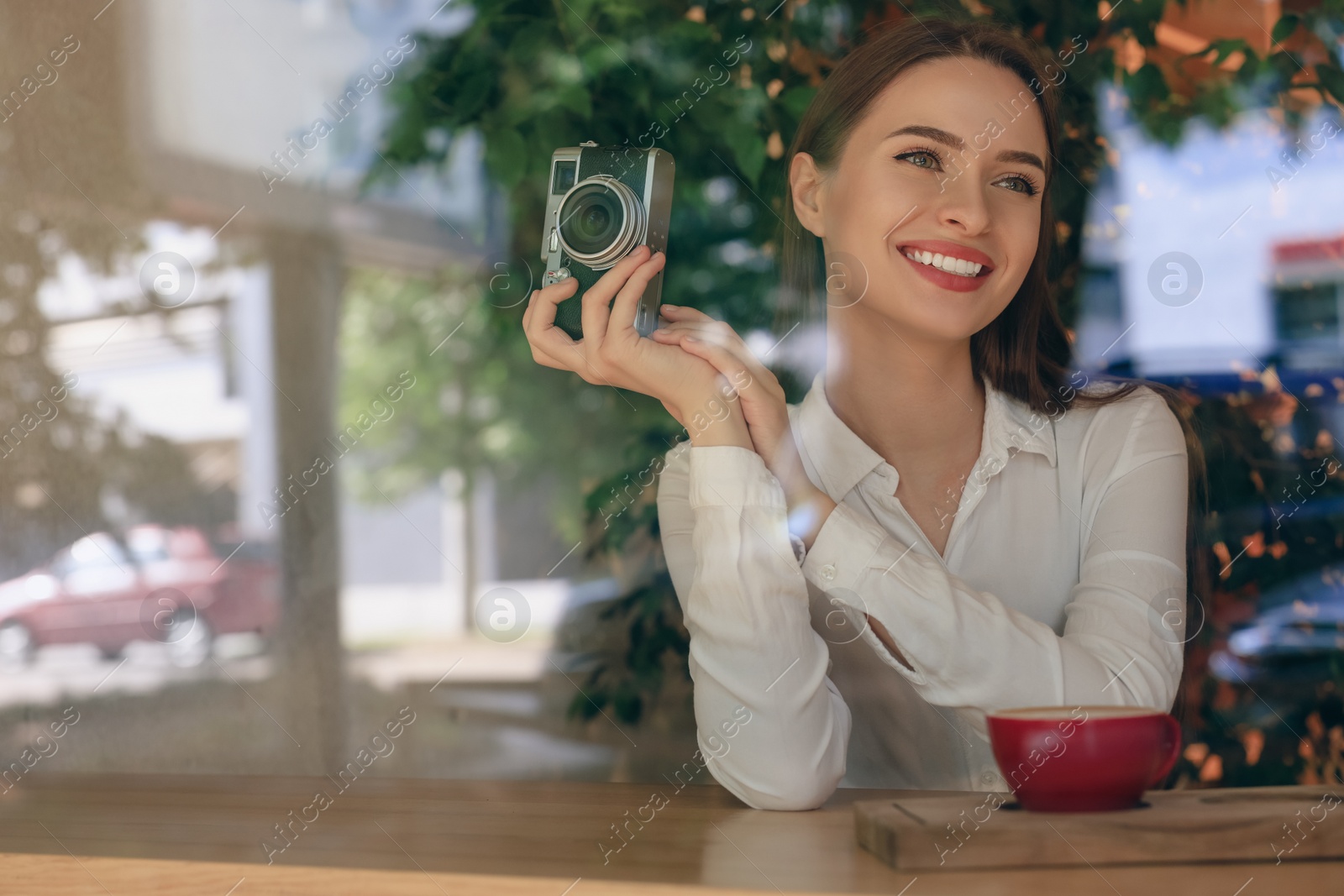 Photo of Young woman with camera and cup of coffee at cafe, view through window. Creative hobby