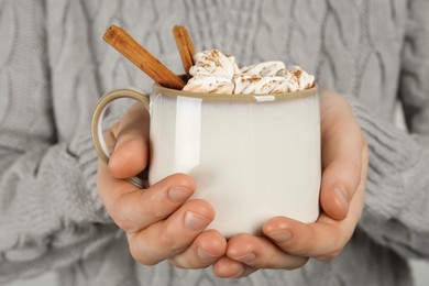 Woman holding cup of delicious hot chocolate with marshmallows and cinnamon sticks, closeup