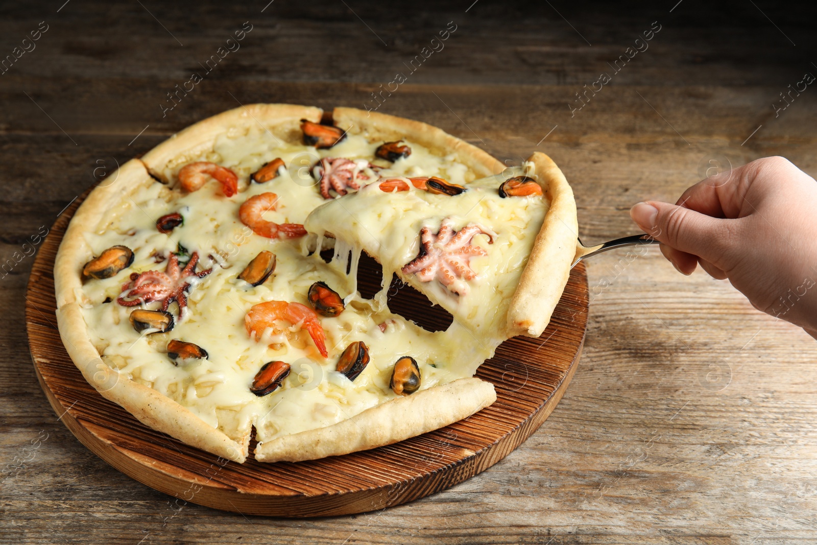 Photo of Woman taking piece of delicious seafood pizza at wooden table, closeup