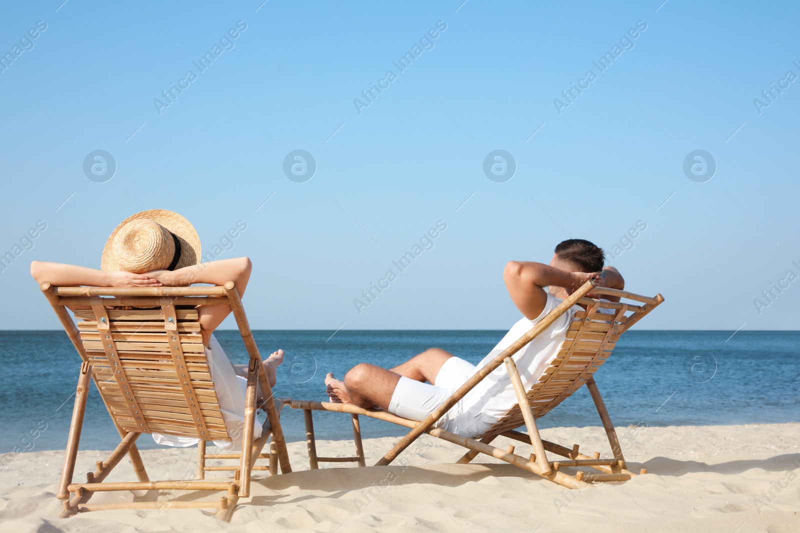 Photo of Young couple relaxing in deck chairs on beach