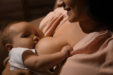 Woman breastfeeding her little baby on sofa in evening