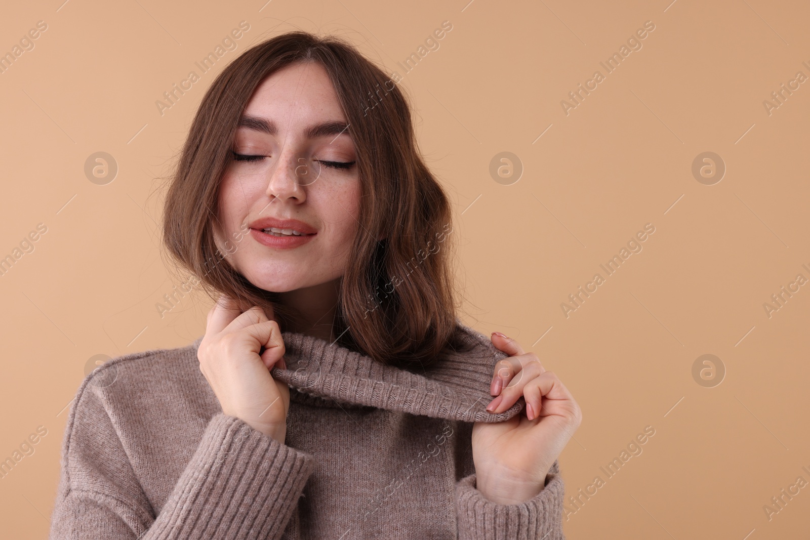 Photo of Portrait of beautiful young woman in warm sweater on brown background, space for text