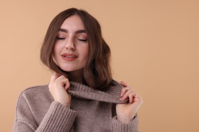 Portrait of beautiful young woman in warm sweater on brown background, space for text