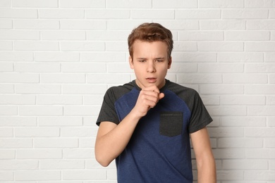 Photo of Teenage boy suffering from cough near brick wall