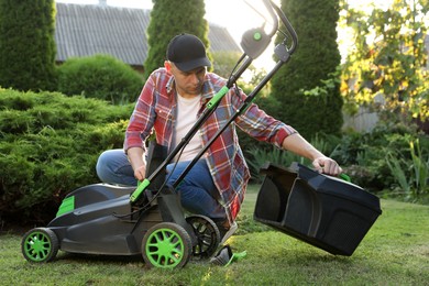 Photo of Cleaning lawn mower. Man detaching grass catcher from device in garden