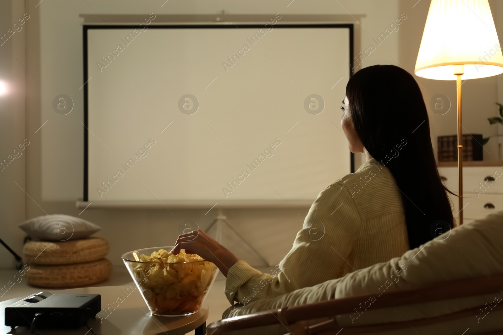 Photo of Young woman watching movie using video projector at home