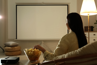 Photo of Young woman watching movie using video projector at home