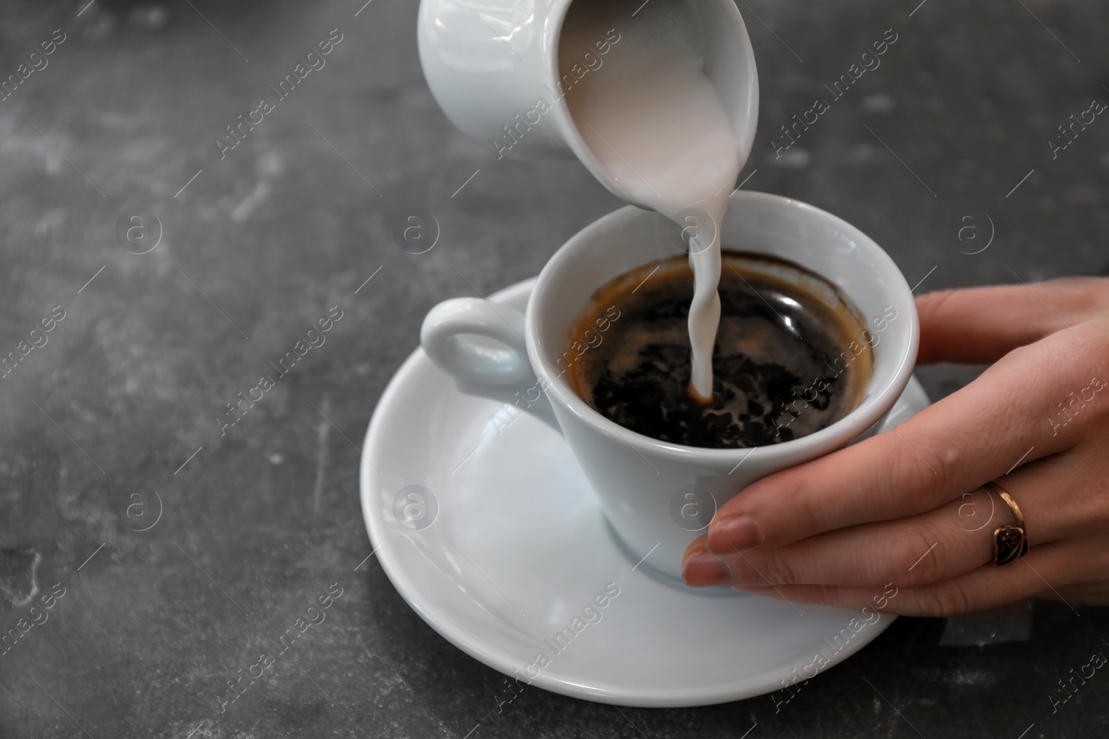 Photo of Woman adding milk to fresh aromatic coffee at table, closeup