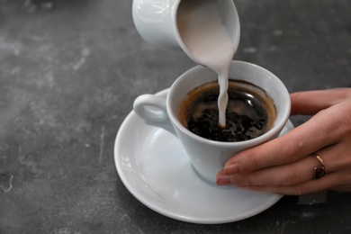 Photo of Woman adding milk to fresh aromatic coffee at table, closeup