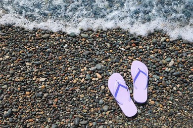 Photo of Stylish lilac flip lops on pebble beach near sea, above view. Space for text