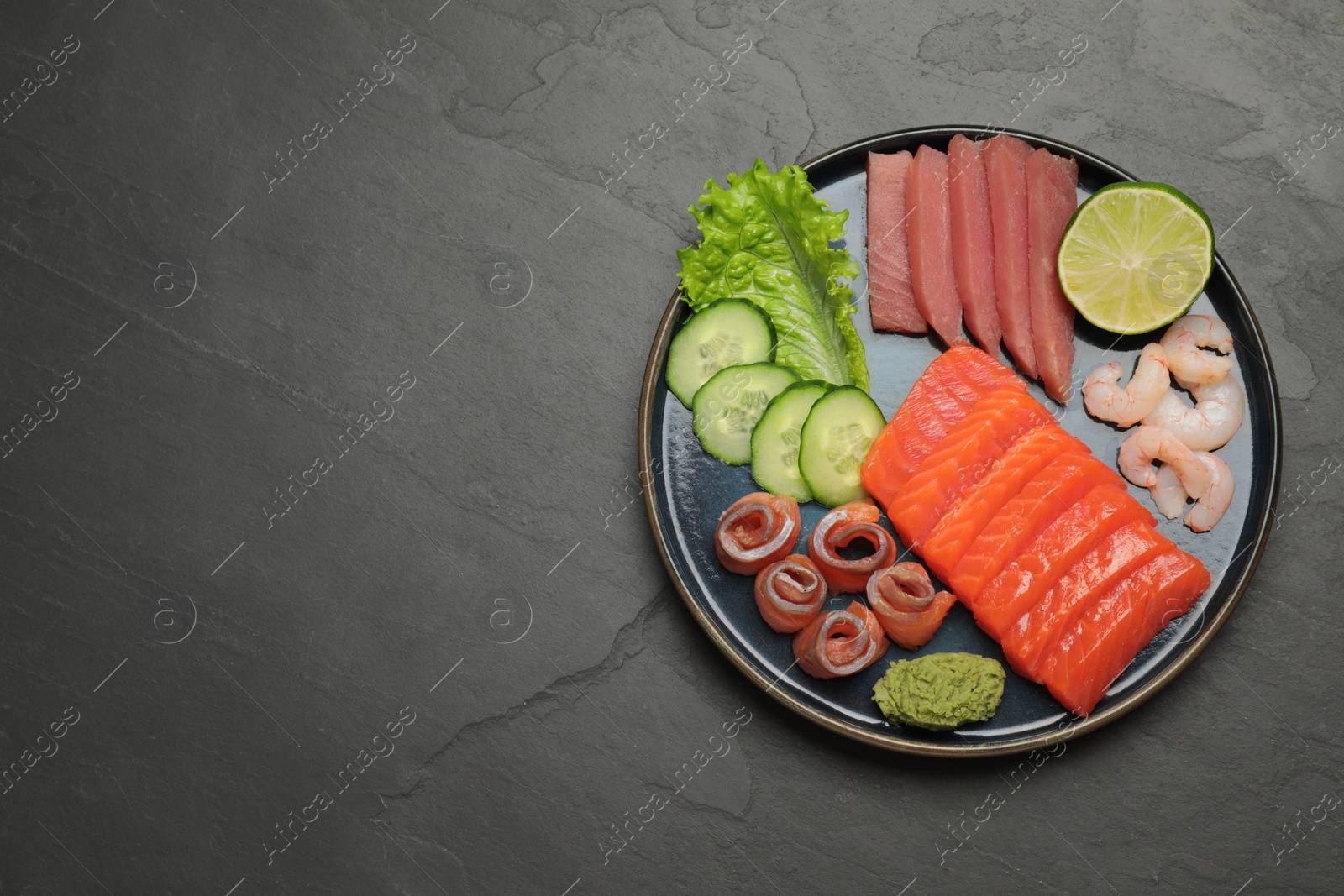 Photo of Tasty salmon slices, shrimp, cucumber and tuna on black table, top view with space for text. Delicious sashimi dish